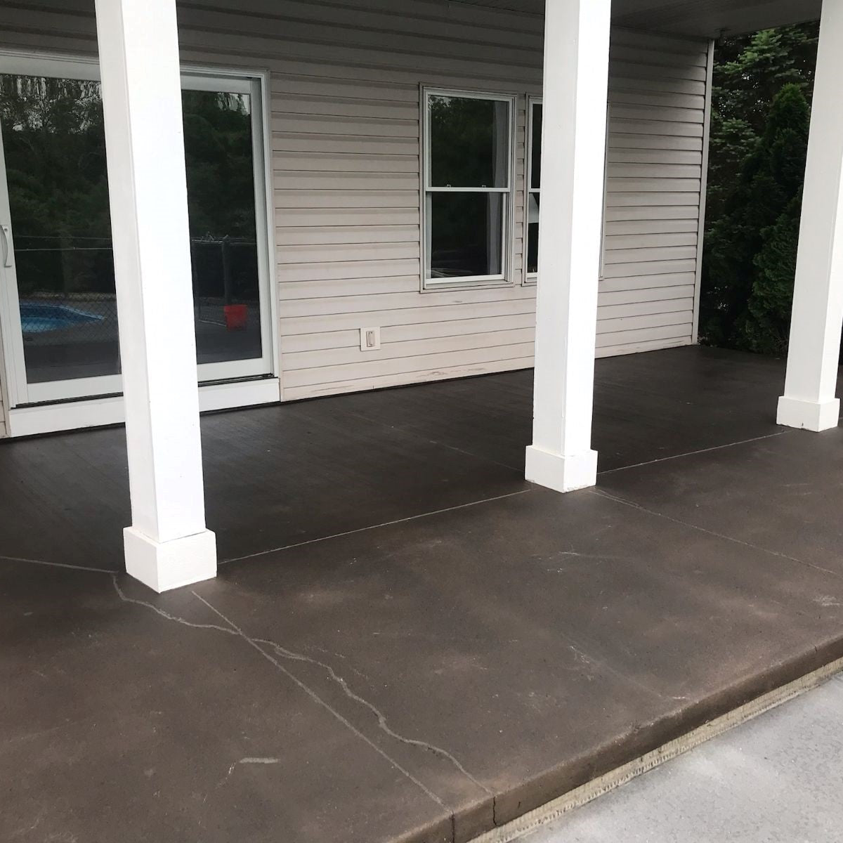 Dark concrete patio with white columns in front of a house